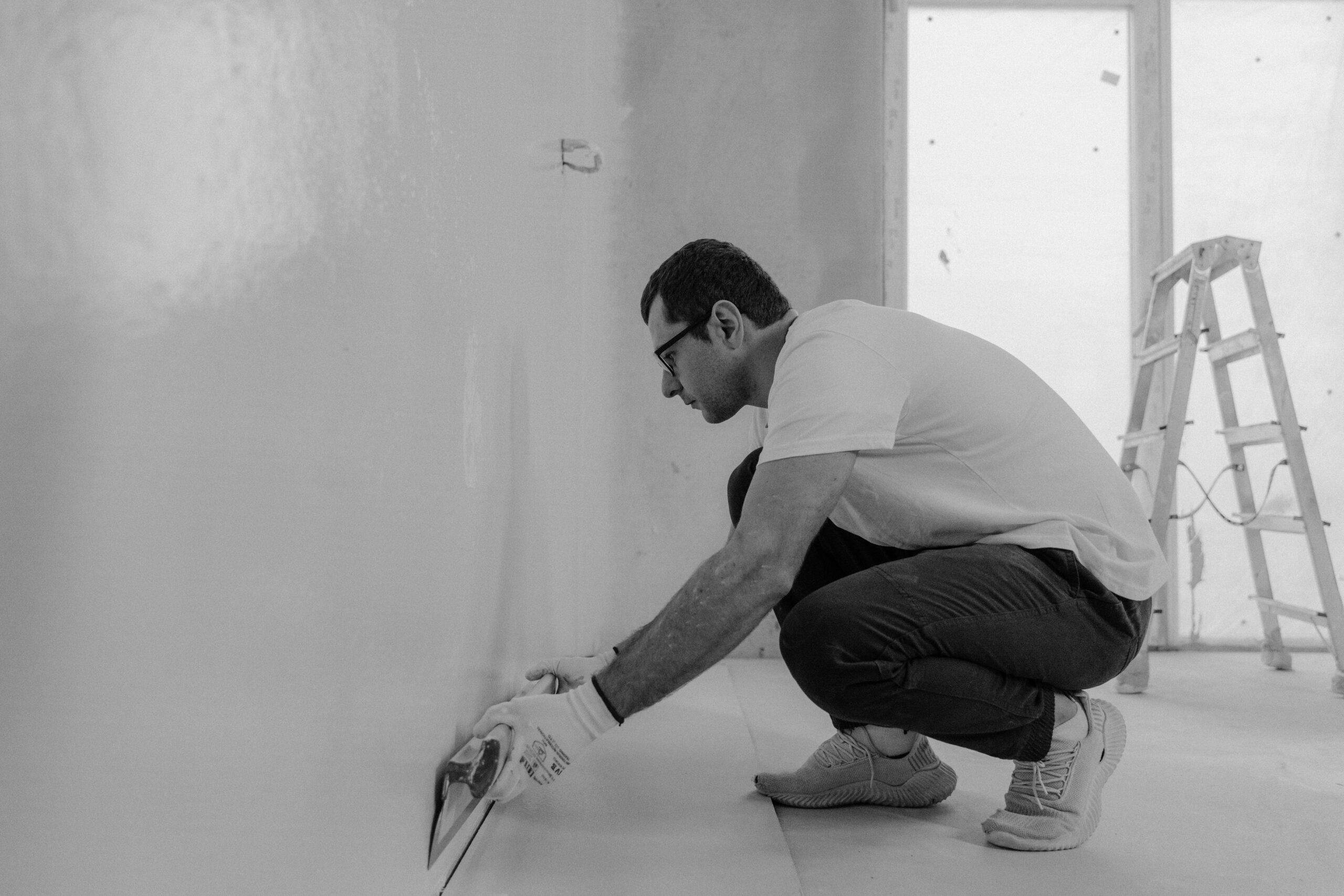 Monochrome image of a man renovating an interior wall using plaster tools.